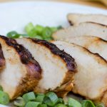 Sliced chicken breast on a white plate, garnished with chopped green onions.