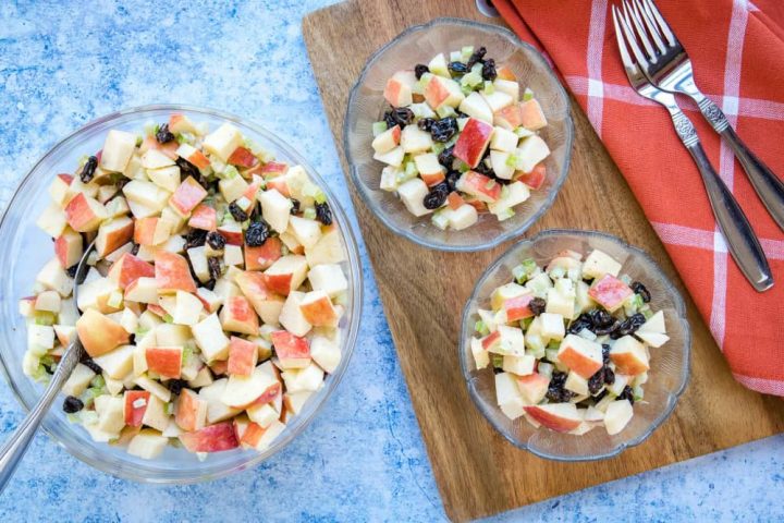 Overhead view of salad with chopped apples, raisins, and celery with a coral plaid towel and two forks.