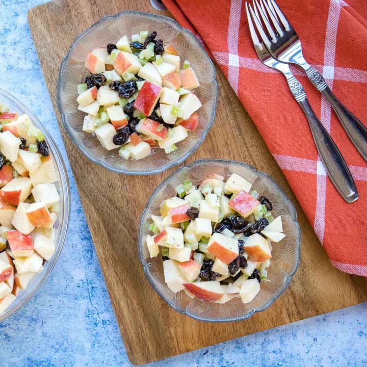 Overhead view of salad with chopped apples, raisins, and celery with a coral plaid towel and two forks.