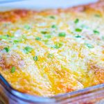 Clear baking dish with enchiladas covered with cheese and diced green onions.