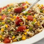 Ground beef, corn, peas, diced tomotoes, and ramen noodles on a white plate.