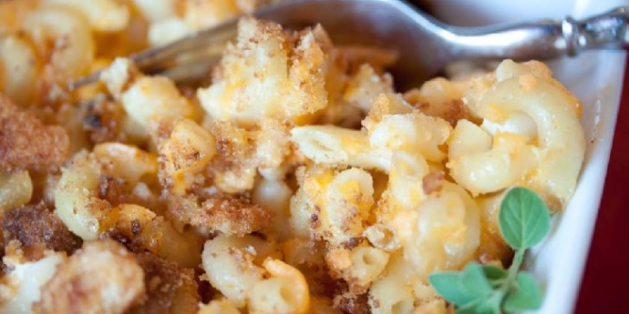 A single serving of macaroni & cheese with a bread crumb topping with a fork and garnished with fresh thyme