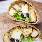 Diced chicken, sliced black olives, lettuce, and pesto wrapped in a tortilla. The wrap is on top of another similar wrap, next to some pesto on a white plate.