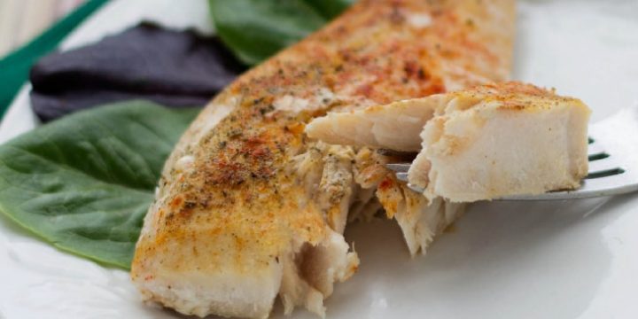 Seasoned fish filet on a white plate with a fork lifting one bite.