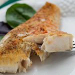 Seasoned fish filet on a white plate with a fork lifting one bite.