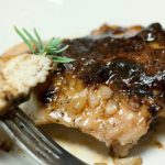 Chicken breast covered in a brown sugar sauce on a white plate. There is a fork holding a small piece of chicken