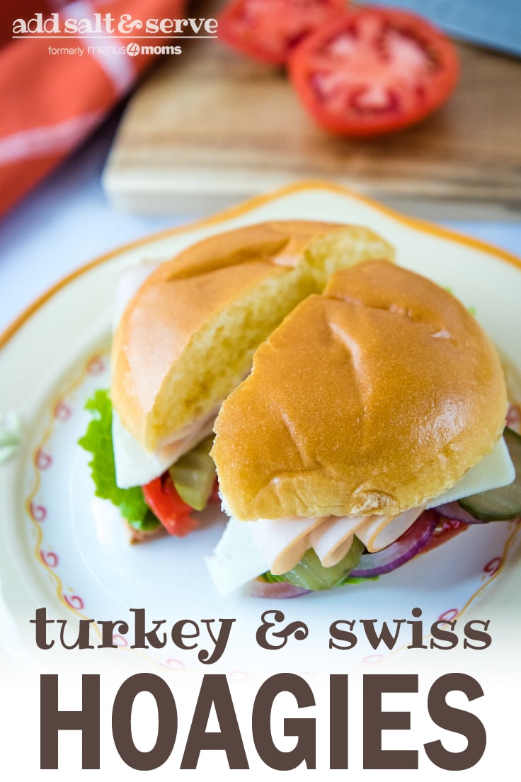 Brioche bun with slices of turkey, Swiss cheese, lettuce, tomato, pickle, and onion on a white and orange plate with cutting board and tomato in the background; text Turkey & Swiss Hoagies Add Salt & Serve (formerly Menus4Moms)