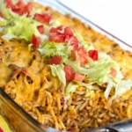Clear casserole dish with spaghetti noodles, ground beef, and melted cheese, topped with shredded lettuce and diced tomatoes.