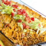 Clear casserole dish with spaghetti noodles, ground beef, and melted cheese, topped with shredded lettuce and diced tomatoes.