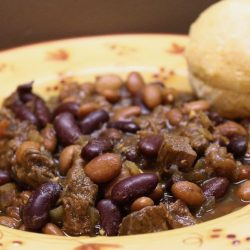 Kidney beans, pinto beans, and diced beef in a broth, all in a yellow soup bowl with red flowers. There is a biscuit on the rim of the bowl.