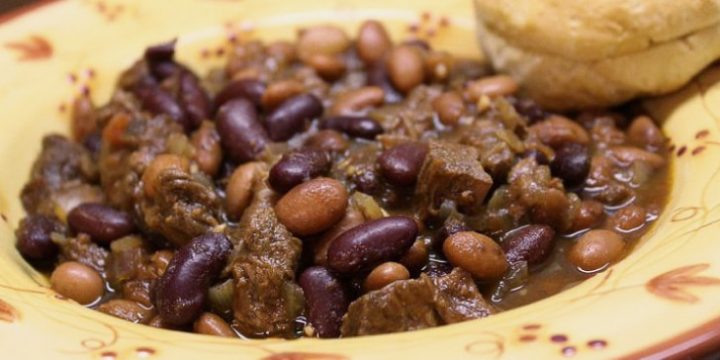 Kidney beans, pinto beans, and diced beef in a broth, all in a yellow soup bowl with red flowers. There is a biscuit on the rim of the bowl.
