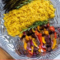 Large pewter platter of yellow rice, grilled asparagus, and grilled beef kabobs with bell peppers, red onions, and mushrooms with text Beef & vegetable kabobs Add Salt & Serve