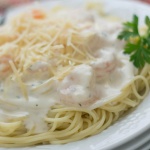 Angel hair pasta with alfredo sauce and shrimp, topped with shredded parmesan cheese, on a white plate.