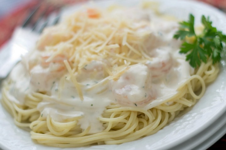 Angel hair pasta with alfredo sauce and shrimp, topped with shredded parmesan cheese, on a white plate.