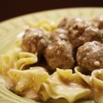 Yellow bowl with egg noodles covered in meatballs with cream sauce
