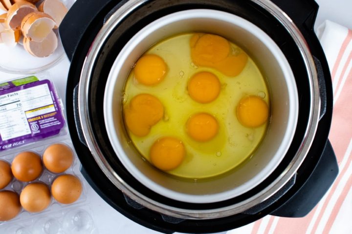 Image showing overhead view of cracked eggs in an inner pot inside Instant Pot with a carton of eggs to the side