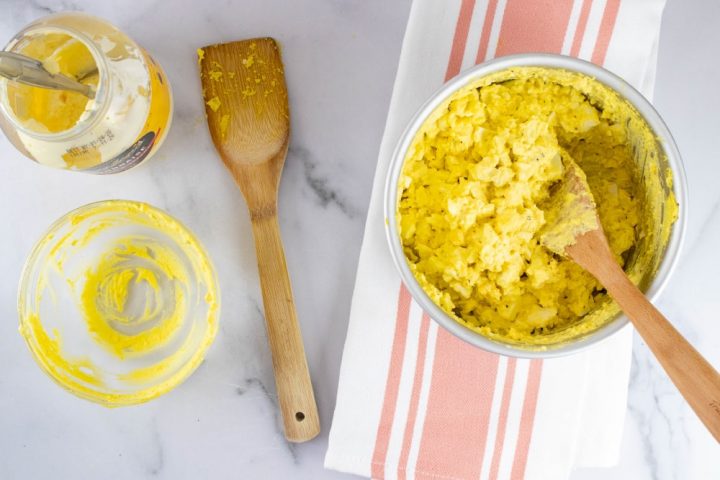 Overhead view of partially prepared egg salad with an open mayonnaise jar and a wooden spoon