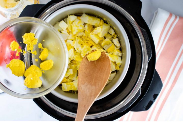 Overhead view of a layer of cooked eggs in an inner pot in an Instant Pot cut into squares with a wooden spoon pulling out some of the cooked yolk