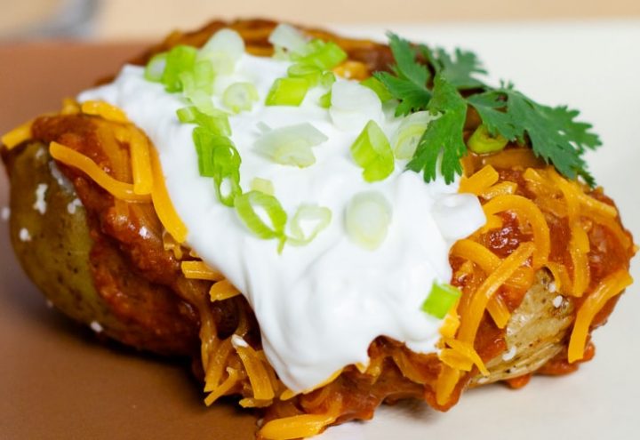 Baked potato topped with chili, shredded cheddar cheese, sour cream, and diced green onions.