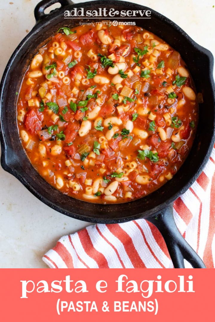 Cast iron skillet with Pasta e Fagioli, a soup made with pasta, tomatoes, chopped celery, onion, and parsley, cannellini beans, and tomato sauce. There's an orange and white striped towel on the counter to the right of the skillet. Text pasta e fagoioli (pasta & beans) add salt & serve formerly menus4moms