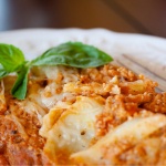 Ravioli mixed with spaghetti sauce and ricotta cheese on a white plate with a fork.