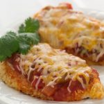 Two chicken breasts coated with cracker crumbs, and topped with salsa and melted shredded cheese, on a white plate.