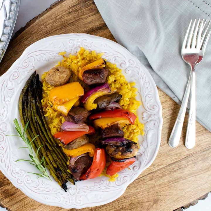 plate of cooked beef and vegetable kabobs over yellow rice served with grilled asparagus
