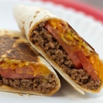 A burrito with ground beef, tomato slices, and melted cheese, cut in half on a white plate.