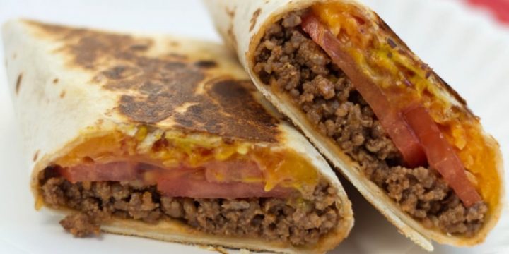 A burrito with ground beef, tomato slices, and melted cheese, cut in half on a white plate.