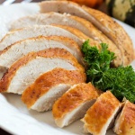 Sliced roasted turkey breast with golden brown skin on a white plate garnished with parsley
