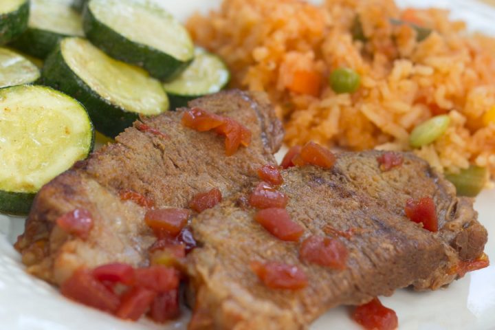 A white plate with sliced cucumbers, two slices of pot roast garnished with diced tomatoes, and Mexican Style Rice.