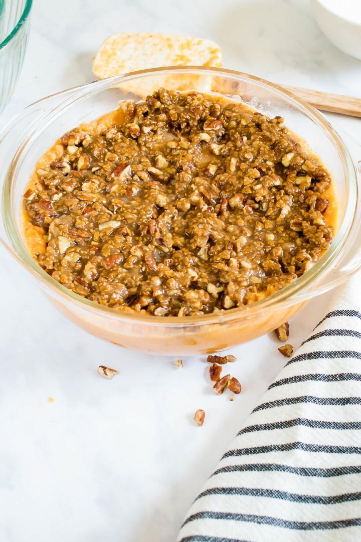 Round glass baking dish with sweet potato casserole and streusel topping ready to be baked