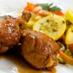 Two chicken drumsticks on a white plate with sliced yellow squash, onions, and bell peppers.