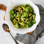 Overhead shot of cooked and seasoned broccoli in a serving bowl with a slotted spoon to the side