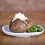 Baked Potato with butter garnished with parsley on a white plate
