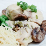Chicken, mushrooms, green peas, and angel hair pasta on a white plate garnished with diced green onions.