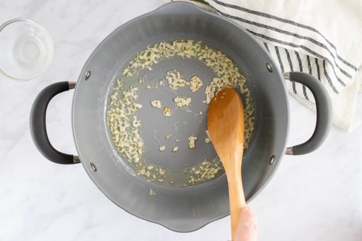 A wooden spoon stirring minced garlic in a pan