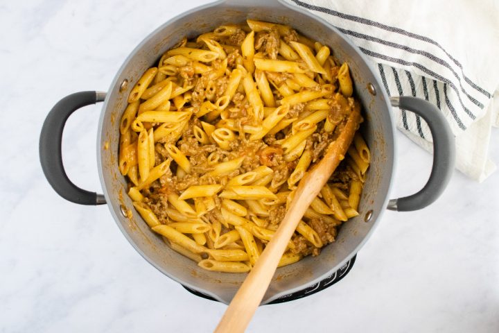 overhead view of cooked penne pasta and cooked ground beef in a creamy sauce in a large pot