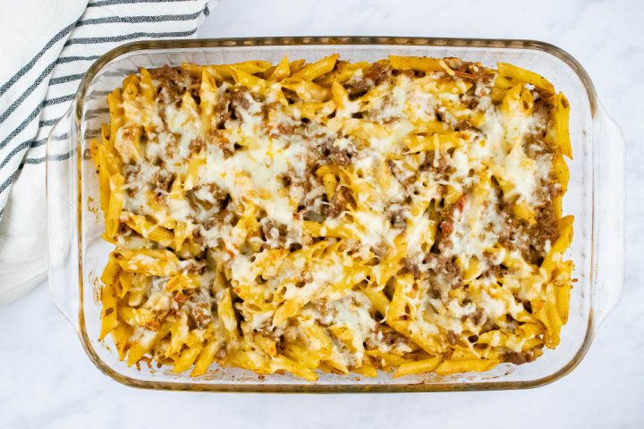 Overhead view of baked penne pasta bake topped with shredded cheese in a glass pan
