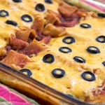Glass casserole dish with enchiladas topped with melted cheese and sliced black olives.