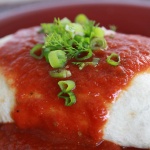 Burrito with red sauce poured over it and garnished with cilantro and chopped green onions