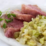 Corned beef and cabbage on a white plate garnished with a sprig of parsley.
