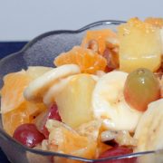 Grapes, chopped oranges, pineapples, and walnuts, and sliced bananas in a bowl.