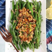 A rectangle white plate of Green Beans Almondine with a serving fork