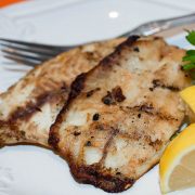White plate with fish fillets garnished with lemon wedges and parsley