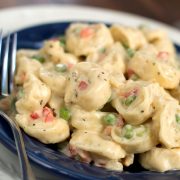 A blue plate with a fork and tortellini, peas, and diced bell peppers covered in cream sauce.