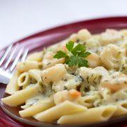 Penne pasta topped with shrimp and a garlic cream sauce on a red plate with a fork.