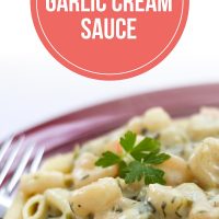 Penne pasta topped with shrimp and a garlic cream sauce on a red plate with a fork with text Shrimp & Garlic Cream Sauce - Add Salt & Serve logo