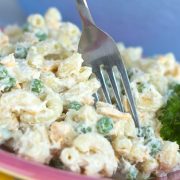 Tuna salad with pasta and peas on a red plate with a fork, garnished with parsley