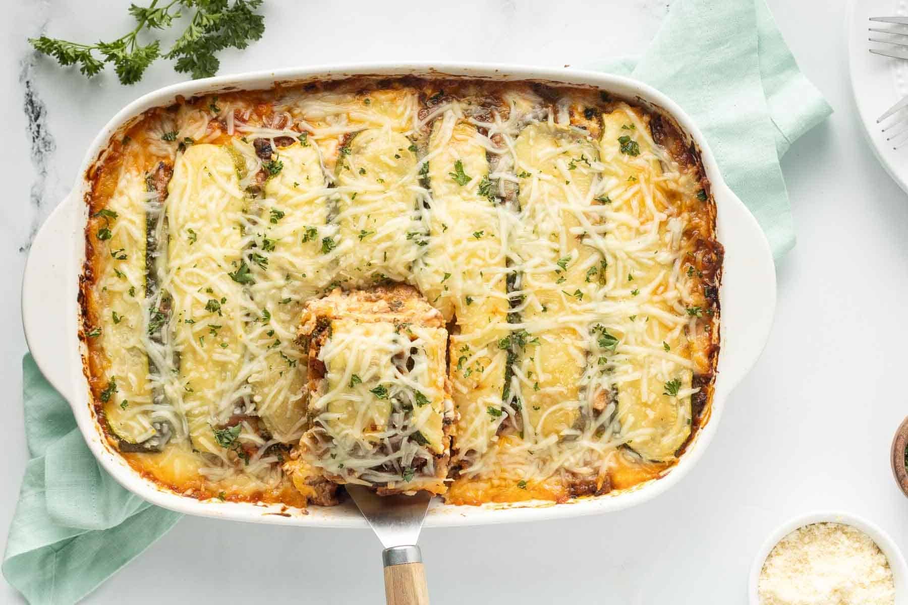 White casserole dish containing Freezer Zucchini Lasagna. Serving spatula is lifting a piece of lasagna out of the pan.